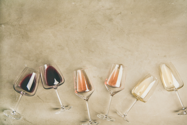 A line up of of 6 wine glasses with red, white and rosé wine lying on their side on a tan floor
